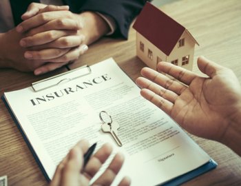 Close-up of a home insurance document on a clipboard with two people discussing terms at a table, symbolizing trust, security, and professionalism in home services