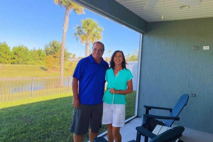 Sharon and Mark from In the Bubble Home Watch standing together on a screened lanai overlooking a peaceful Florida backyard with palm trees and blue skies
